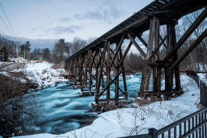 Old wooden rail bridge over a rushing river that was partly frozen