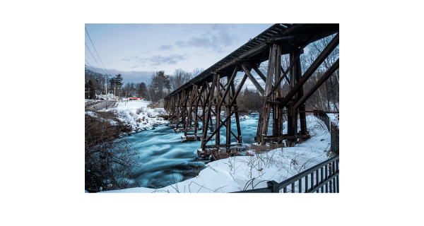 Old wooden rail bridge over a rushing river that was partly frozen